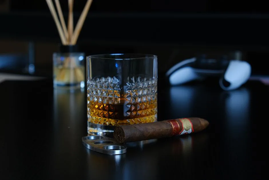 A glass of whisky with a cigar on a dark tabletop, embodying luxury and relaxation.
