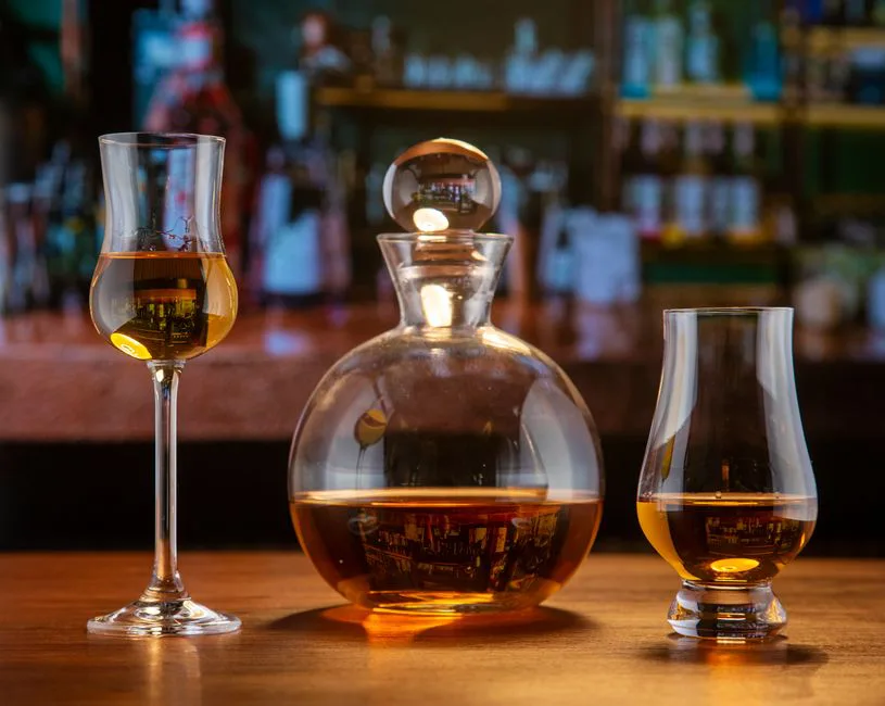 Close-up of elegant glassware with amber liquor set on a wooden bar counter.