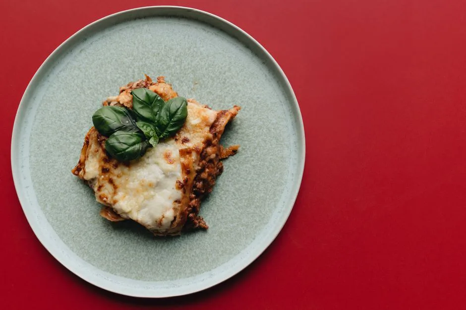 Delicious Italian lasagna topped with fresh basil served on a minimalist plate.